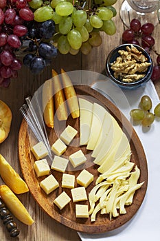 An appetizer of various types of cheese, grapes and walnuts, served with wine. Rustic style.