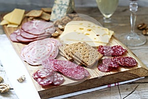 Appetizer of various types of sausages, meats, cheeses and crackers on a wooden board, served to wine