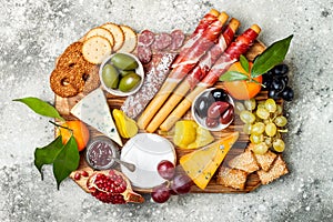 Appetizers table with antipasti snacks. Cheese and meat variety board over grey concrete background. Top view, flat lay.