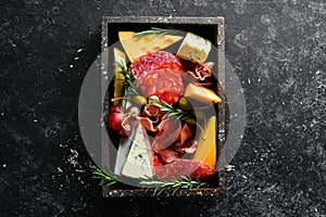 Appetizers table with italian antipasti snacks and wine in glasses. Cheese, wine, salami and prosciutto on a black stone