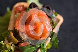 Appetizing appetizer of canape, red fish, salad in a restaurant on a dark black concrete background. Stone Tray.