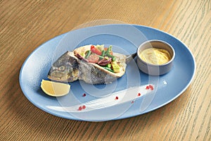 Appetizing baked dorado fish with vegetables tomatoes, asparagus, avocado with yellow sauce on a blue plate on a wooden