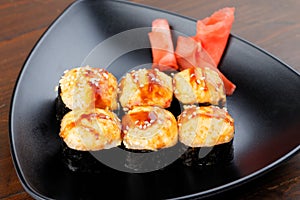 Appetizing baked hot sushi rolls. Set sushi on a black plate with ginger.