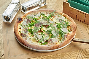Appetizing baked pizza with wild mushrooms, parmesan and arugula with crispy crust on a wooden background. Restaurant table