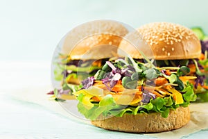 Appetizing burger from fresh sesame buns and raw vegetables and young sprouts on a blue light background. Vegetarianism.