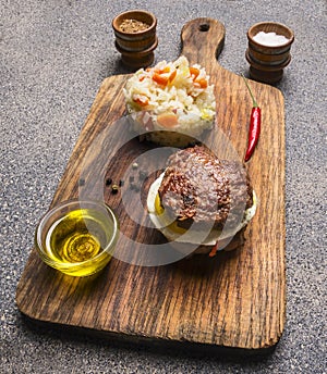 Appetizing burger only meat and eggs and butter, with rice and vegetables, spices on vintage cutting board