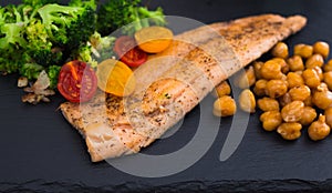 Appetizing cooked trout, chickpeas, broccoli on ack warm stone plate