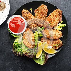 Appetizing crispy chicken wings breaded with bread crumbs with lettuce, sauce, lemon, microgreens in a plate on the