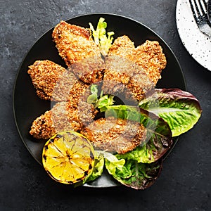 Appetizing crispy chicken wings breaded with bread crumbs with lettuce, sauce, lemon, microgreens in a plate on the