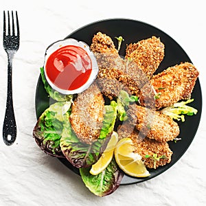 Appetizing crispy chicken wings breaded with bread crumbs with lettuce, sauce, lemon, microgreens in a plate on the