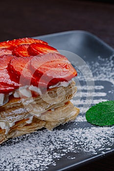 Appetizing dessert of strawberries and puff pastry with cream on a plate. mint leaves.close up. side view