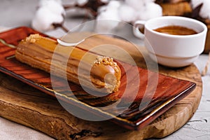 Appetizing eclair with caramel glaze and peanuts and coffee