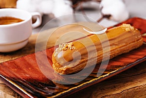 Appetizing eclair with caramel glaze and peanuts and coffee