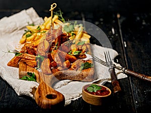 Appetizing fried potato wedges on a wooden cutting board. Big portion of baked potatoes with sauce and herbs. Homemade french