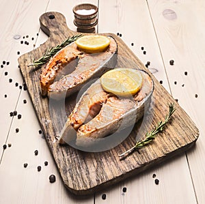 Appetizing fried salmon steak on a cutting board with lemon , rosemary and pepper unground close up