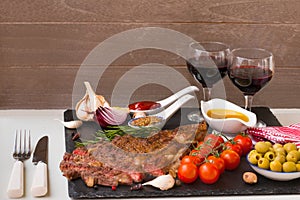 Appetizing grilled meat. Grilled beef entrecote medium roast on black stone board, red wine and two full wine glasses. Best dinner