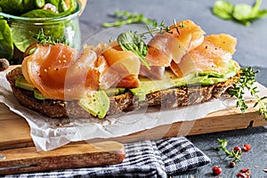 Appetizing and healthy smoked salmon with avocado and vegetables spinach sprouts, tomatoes, thyme on toast. Homemade look