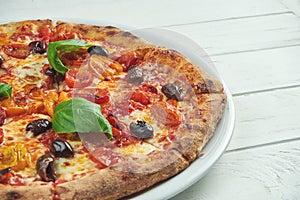 Appetizing, homemade pizza with margarita with cherry tomatoes, basil and mozzarella on a white plate on a white wooden background