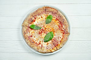 Appetizing, homemade pizza with margarita with tomatoes, basil and mozzarella on a white plate on a white wooden background. Close