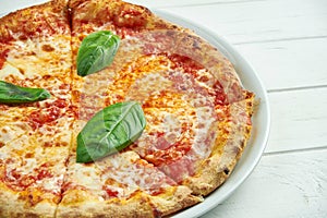 Appetizing, homemade pizza with margarita with tomatoes, basil and mozzarella on a white plate on a white wooden background. Close