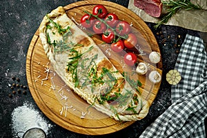 Appetizing italian pizza calzone with different fillings in a composition with ingredients on a wooden board on a black background