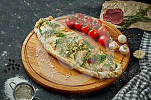 Appetizing italian pizza calzone with different fillings in a composition with ingredients on a wooden board on a black background