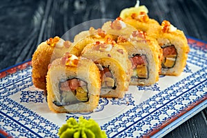 Appetizing Japanese sushi roll in tempura with salmon, avocado and caviar in a blue plate on a black wooden background. Japanese