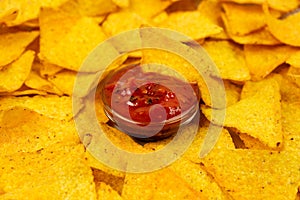 Appetizing nachos chips on a white plate and a spicy sauce close-up.