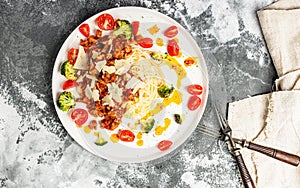 Appetizing pasta with meat in tomato sauce, vegetables and Parmesan cheese in a large white plate. Traditional mediterranean dish