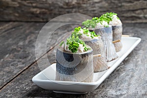 Appetizing pickled herring rolls stuffed with cream cheese and egg mass served on white plate