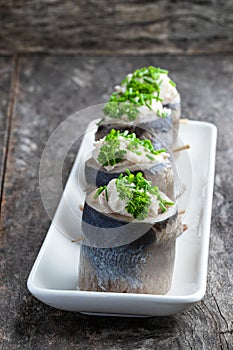 Appetizing pickled herring rolls stuffed with cream cheese and egg mass served on white plate