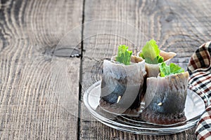 Appetizing pickled herring rolls stuffed with cream cheese and salad leaves on wooden table