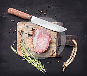 Appetizing piece of raw pork steak on vintage cutting board with herbs and spices for meat a knife on wooden rustic backgroun