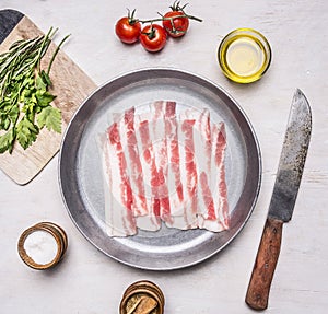 Appetizing pieces of raw bacon in a frying pan with oil, stabbed, herbs, salt and spices wooden rustic background top view clos