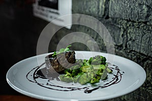 Appetizing pork steak with baked broccoli in red wine sauce on a table in a vintage restaurant. Hot delicious lunch for gourmets