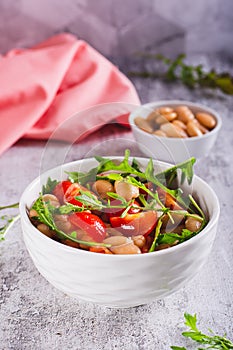 Appetizing salad of canned white beans, cherry tomatoes and arugula in a bowl vertical view