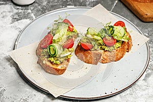 Appetizing sandwiches with avocado, cucumber, cherry tomatoes and herbs. Toast with guacamole sauce and fresh vegetables.