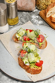 Appetizing sandwiches with guacamole sauce and fresh vegetables. Toast with avocado, cucumber, cherry tomatoes and herbs.