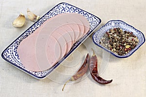 Appetizing sausage sliced on a grey plate on a rough linen background with chilli pepers and spices  close up