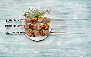 Appetizing shish kebab on a plate with lettuce and rosemary on a blue wooden background.