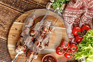 Appetizing shish kebab from pork laid out on a wooden board with fresh vegetables. Still-life on a wooden background.