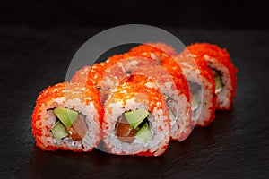 appetizing sushi roll california with avocado shrimp cheese and masago caviar on a black background.