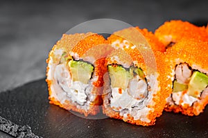 Appetizing sushi roll california with avocado shrimp cheese and masago caviar on a black stone plate
