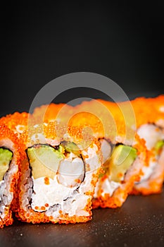 Appetizing sushi roll california with avocado shrimp cheese and masago caviar on a black stone plate