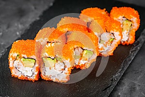 Appetizing sushi roll california with avocado shrimp cheese and masago caviar on a black stone plate