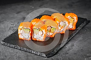 Appetizing sushi roll california with avocado shrimp cheese and masago caviar on a black stone plate