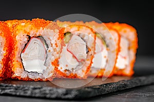 Appetizing sushi roll california with cheese cucumber crab and masago caviar on a black stone plate