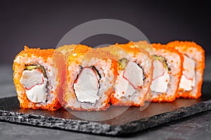 Appetizing sushi roll california with cheese cucumber crab and masago caviar on a black stone plate