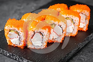 Appetizing sushi roll california with cheese cucumber crab and masago caviar on a black stone plate
