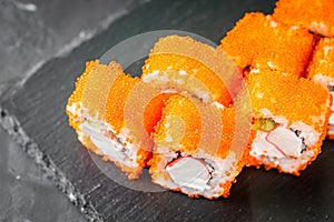 Appetizing sushi roll california with cheese cucumber crab and masago caviar on a black stone plate